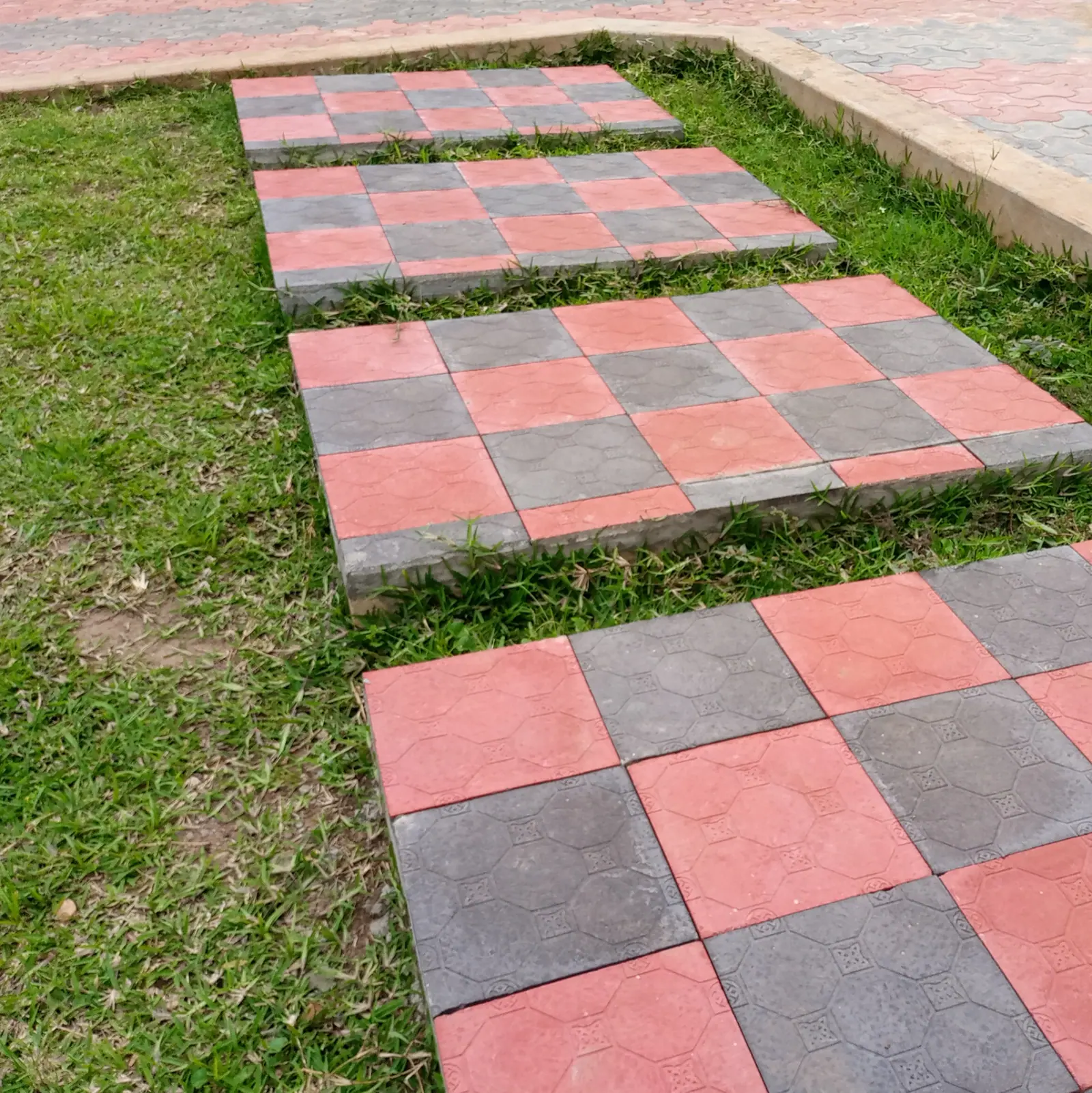 Red and grey walking slabs are separated by strips of grass.
